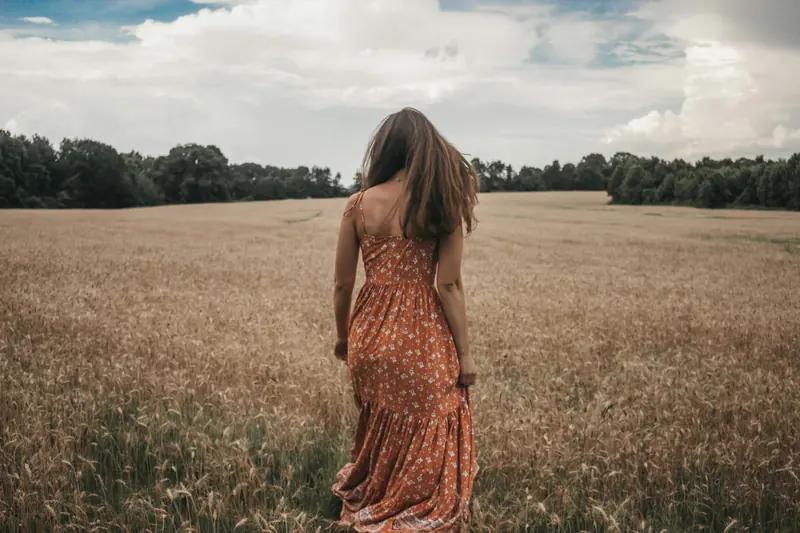 A woman in a long dress walking into a wheat field