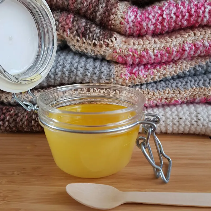 A glass jar of golden oil beside folded blankets