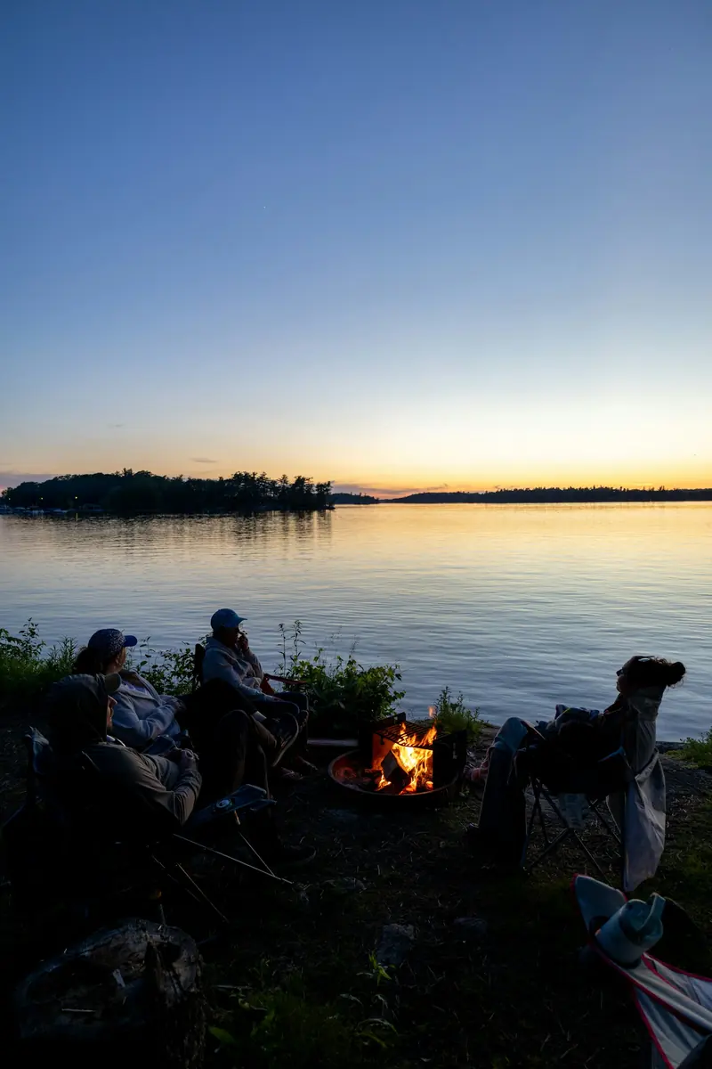 Friends around a campfire by a lake at sunset