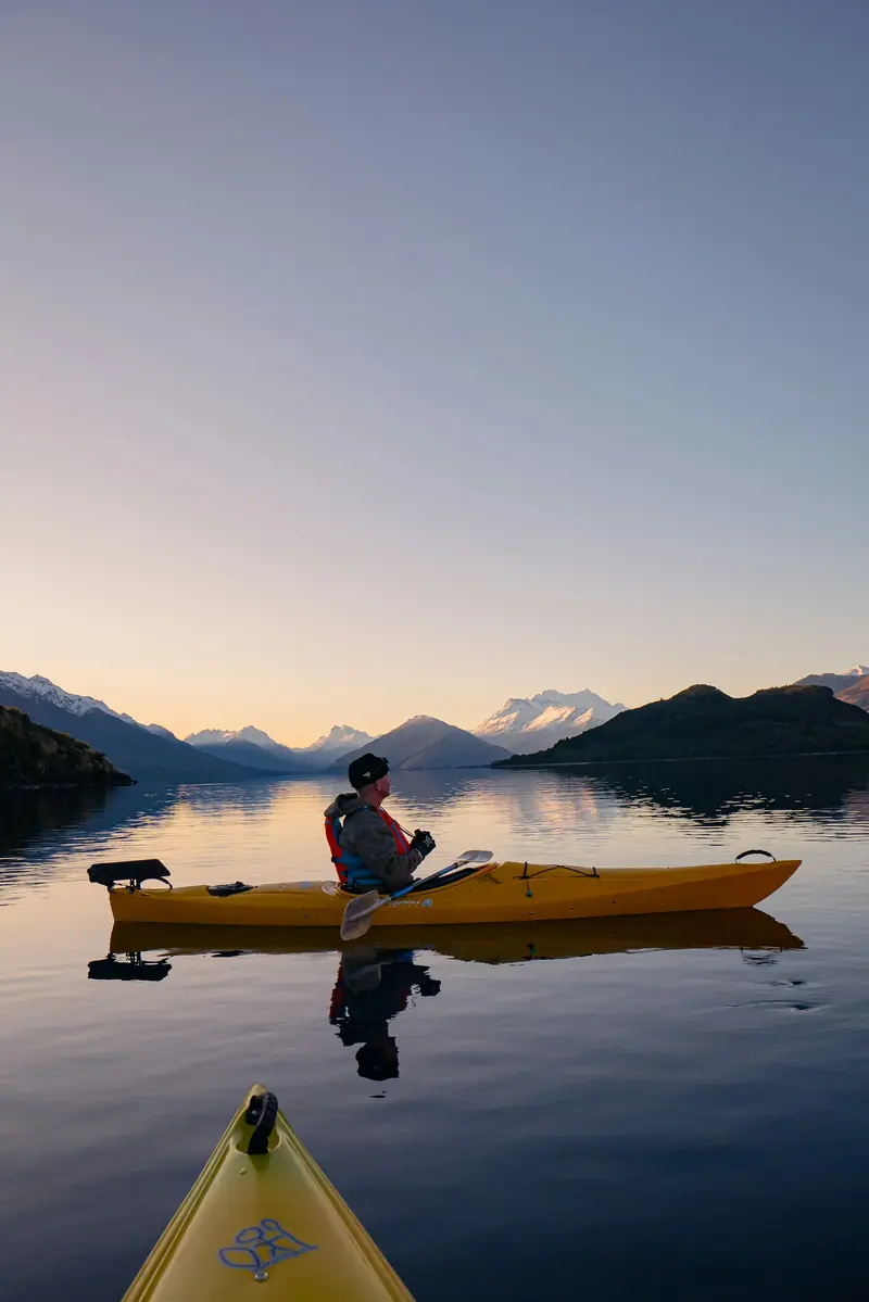 A man paddling a yellow kayak on a calm lake at sunset