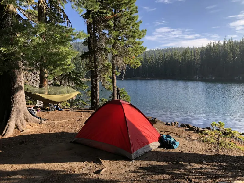 A red tent and a hammock in the pines by a lake