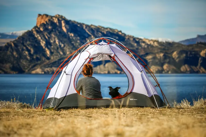 A woman and her dog sitting in an open tent above a lake