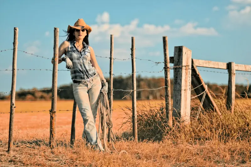 A woman in a cowboy hat leaning on a barbed wire fence