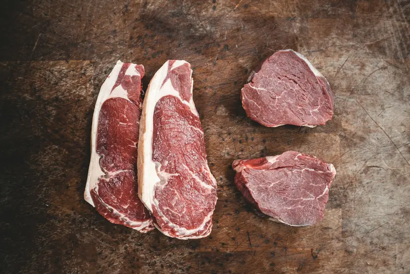 Raw steaks laid out on a dark wooden table