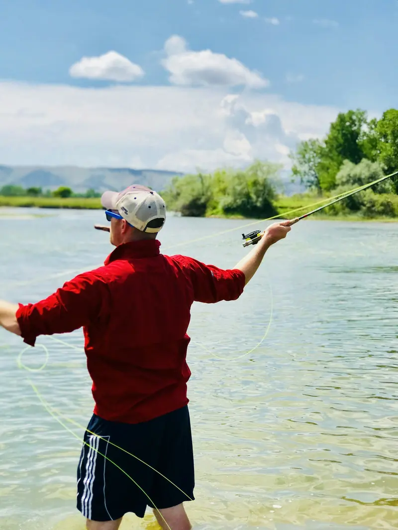 A man in a red jacket casting a fly rod over clear water