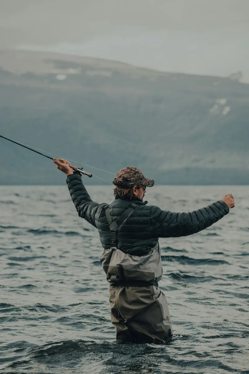 A fly fisherman in waders casting into gray water