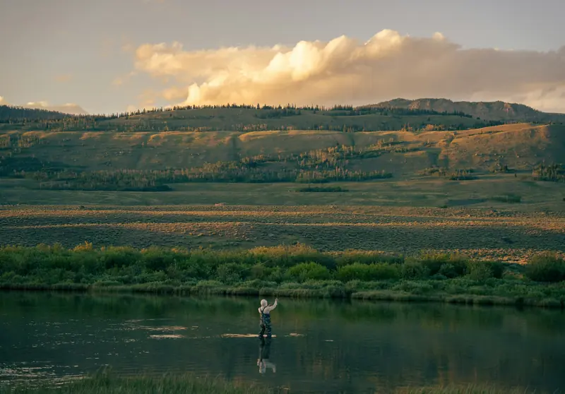 An angler wading a wide river in a golden valley