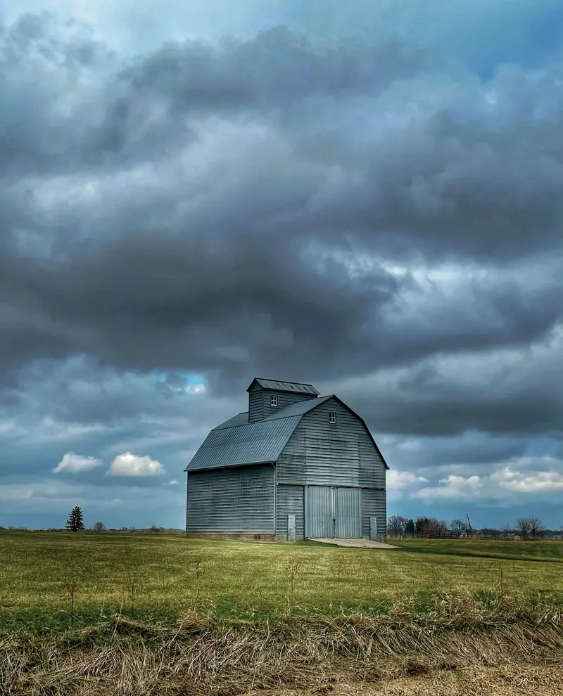 A gray barn alone in a field under heavy clouds