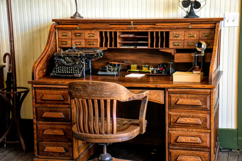 A roll-top desk with a typewriter and a wooden chair