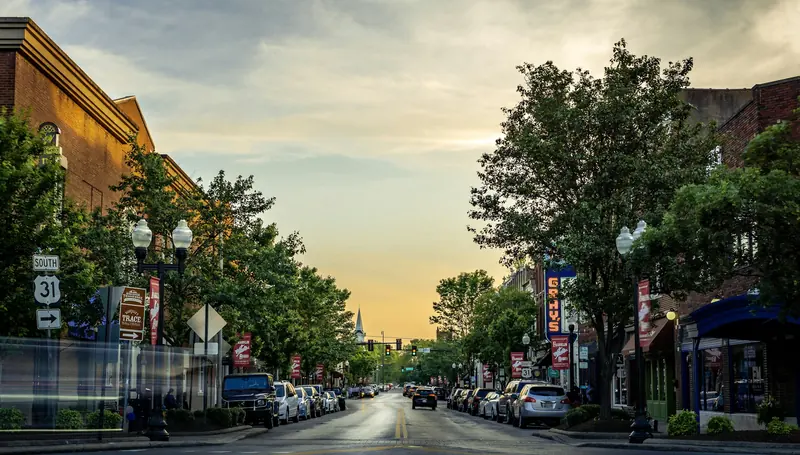 A small-town main street lined with trees and brick storefronts at sunset