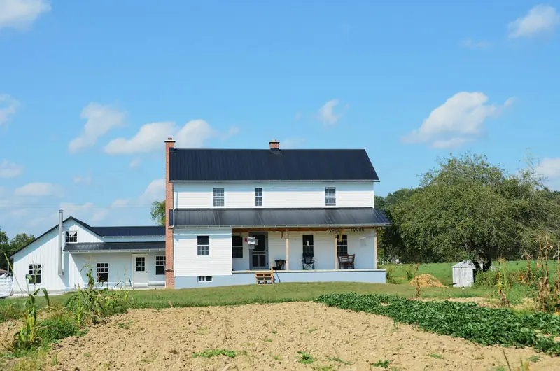 A white farmhouse with a black metal roof and a porch