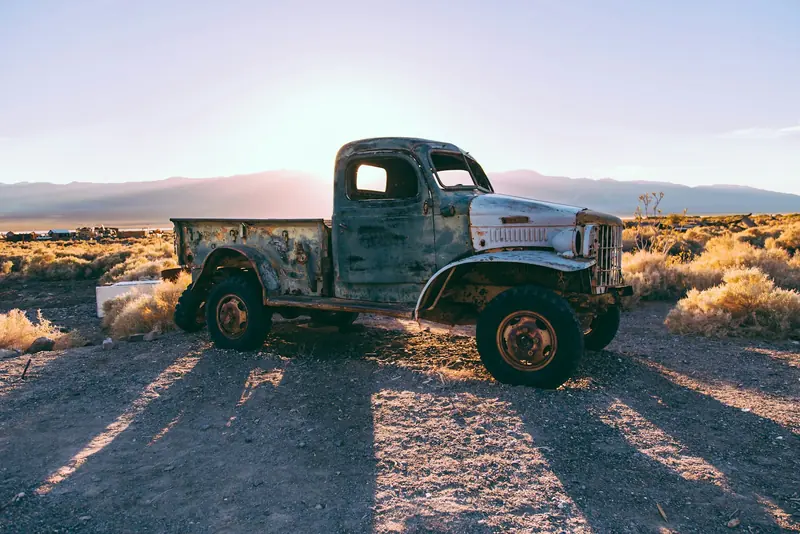 An old single cab pickup parked on a dry ranch yard at sundown