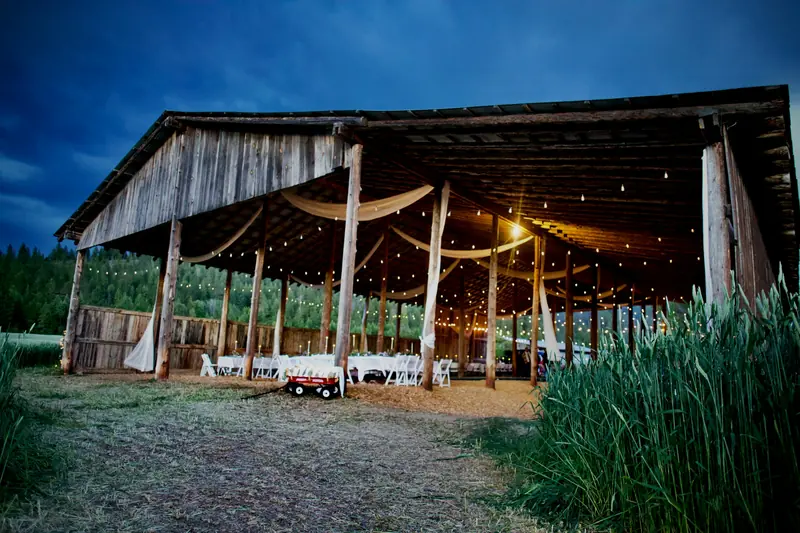An open wooden barn lit with string lights at twilight