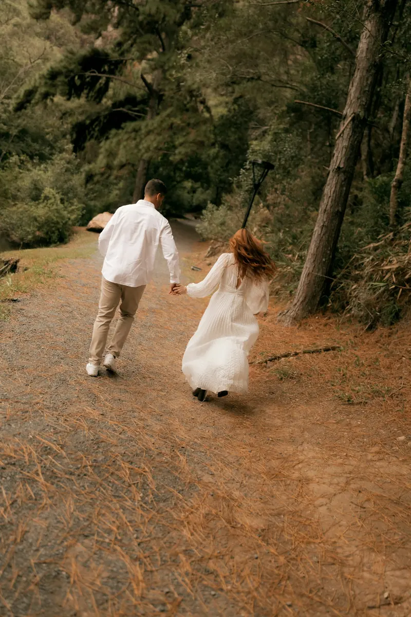 A couple running hand in hand down a forest path
