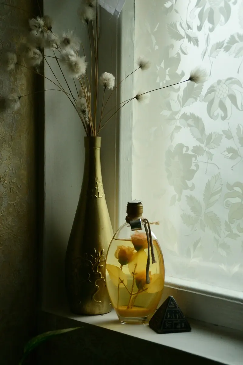 Dried flowers in a gold bottle by a sunny window