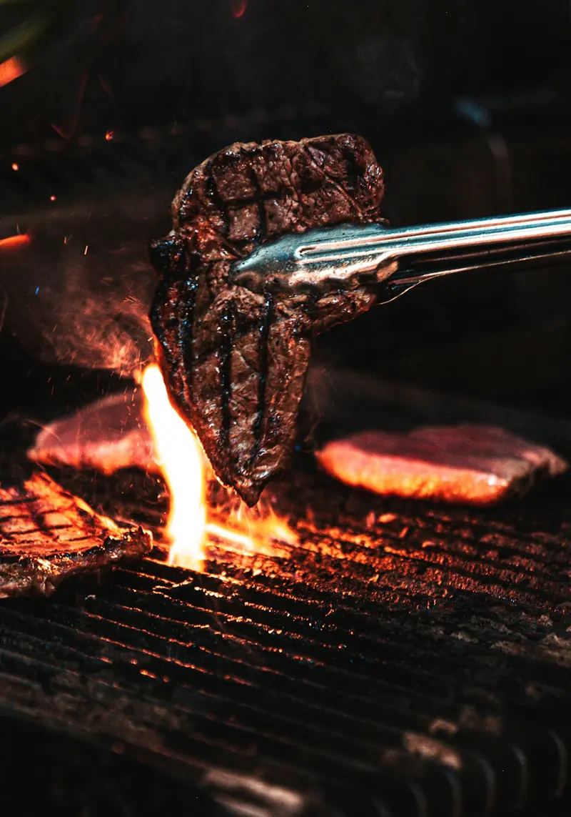 Tongs lifting a steak over the flames