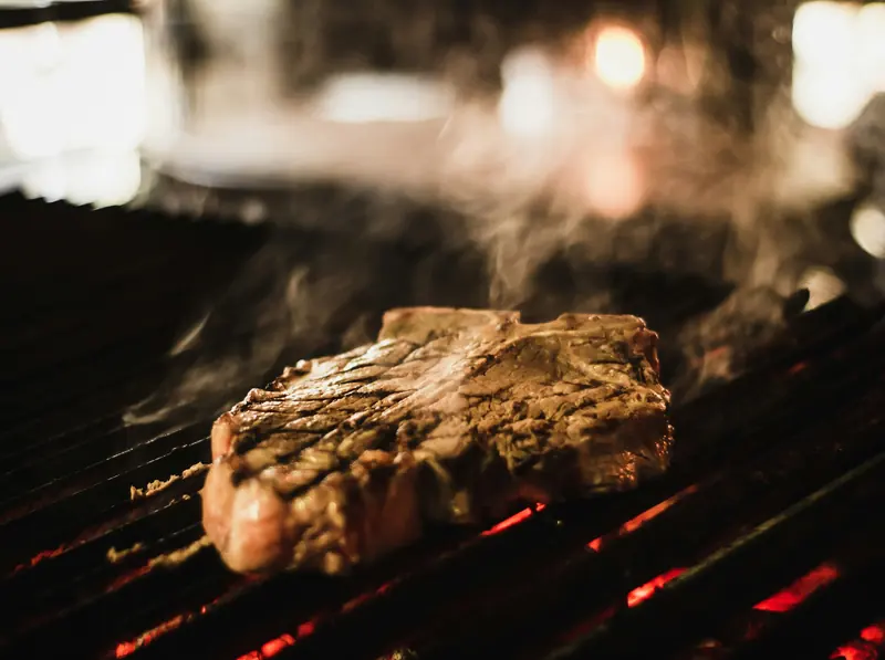 A thick steak searing on a grill in low light