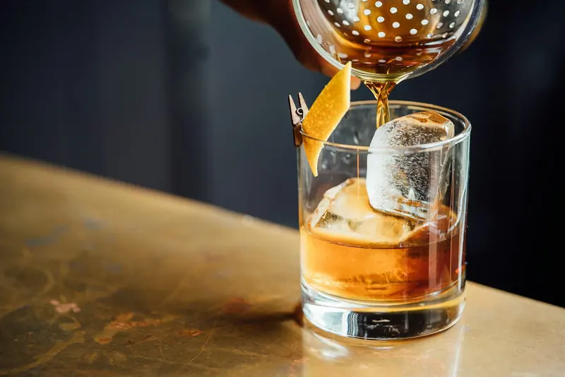 A cocktail poured over a big ice cube