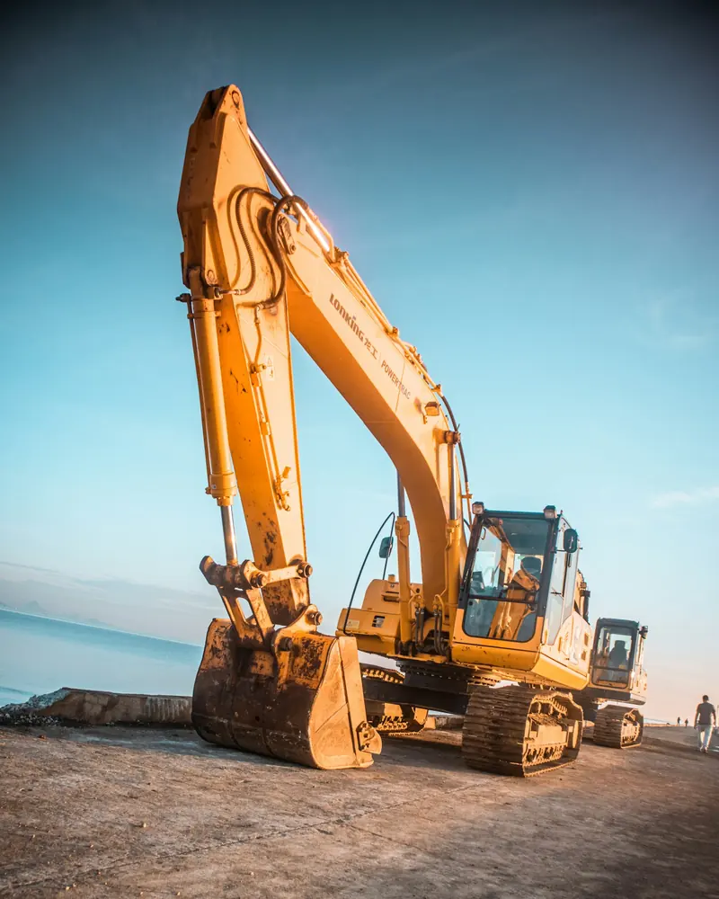 A yellow excavator with its arm raised on a rocky site