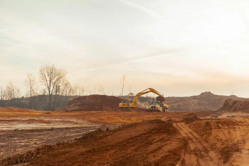 An excavator working on a wide dirt site at sunrise