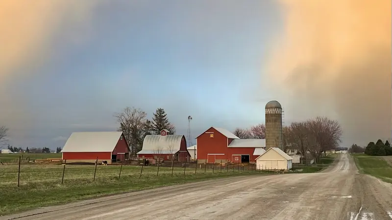 A gravel road leading to a red barn and silo