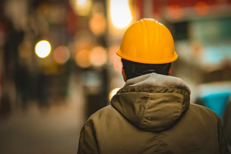 A worker in a yellow hard hat seen from behind