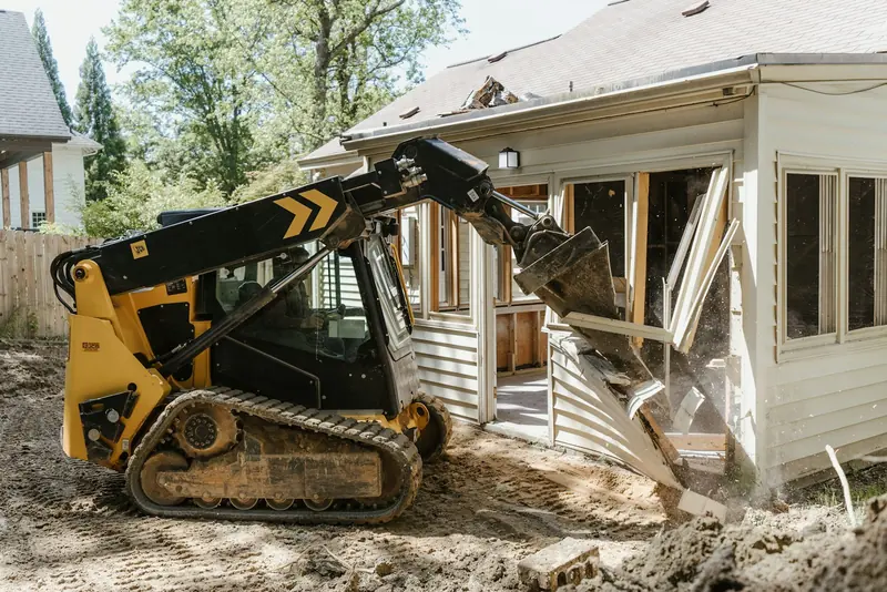 A track loader grading dirt in front of a house