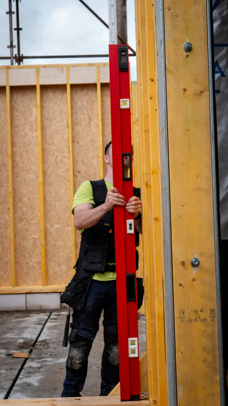 A builder holding a long level against a wall frame