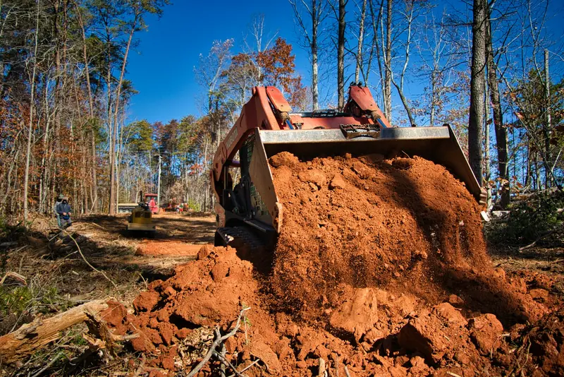 A skid steer moving red dirt in the woods