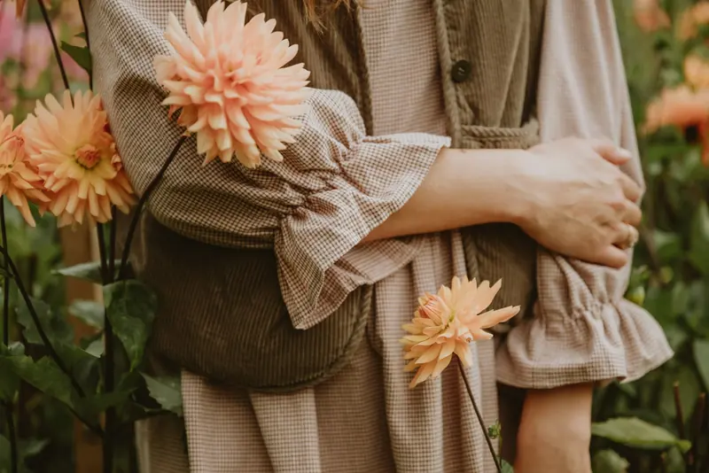 A woman in a gingham dress standing among peach dahlias