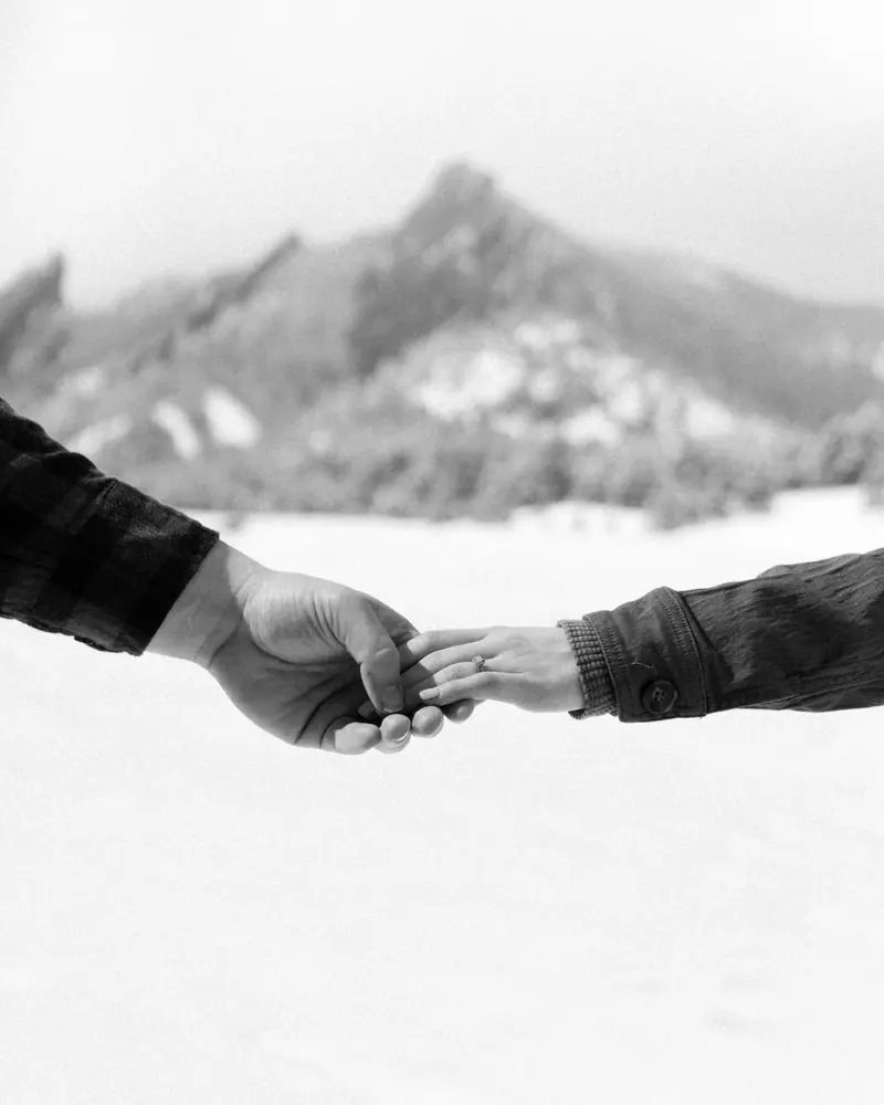 Two hands reaching for each other in front of a snowy mountain