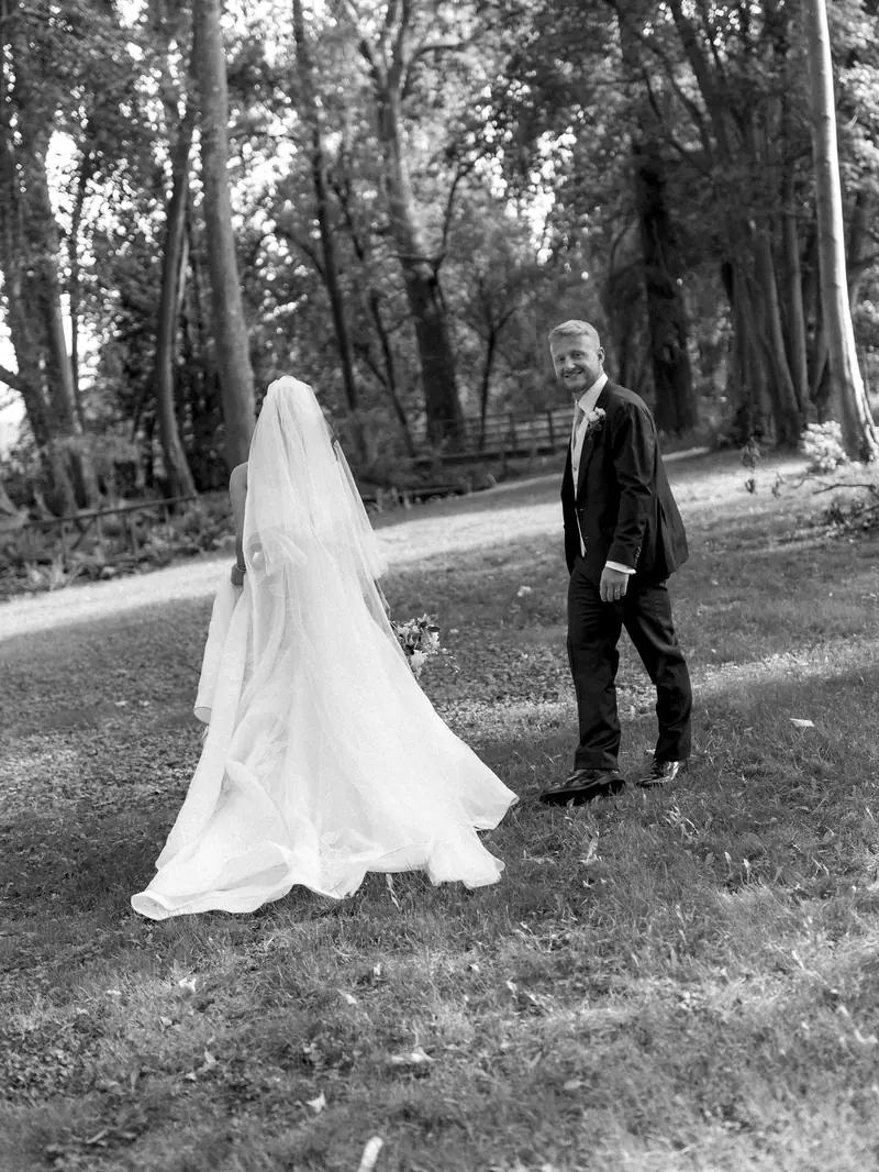 A groom watching his bride walk down a forest trail
