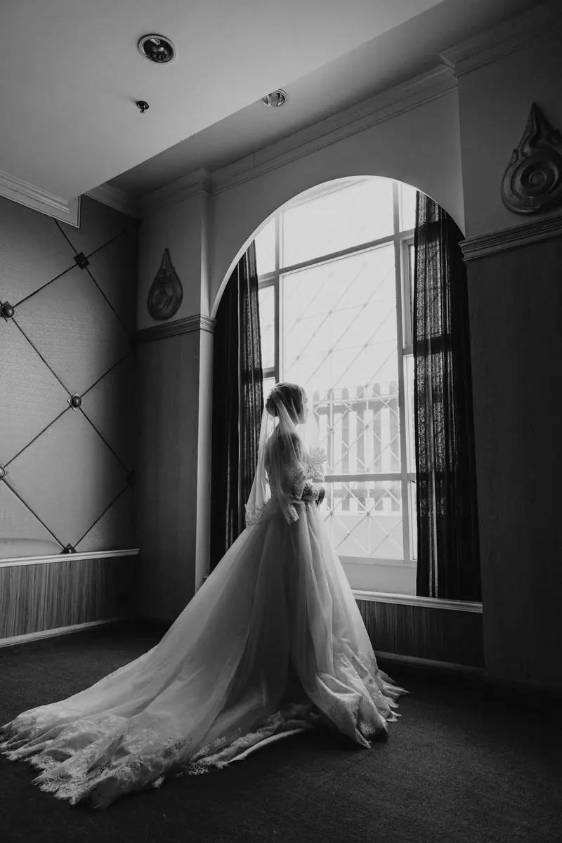 A bride standing in a tall arched window