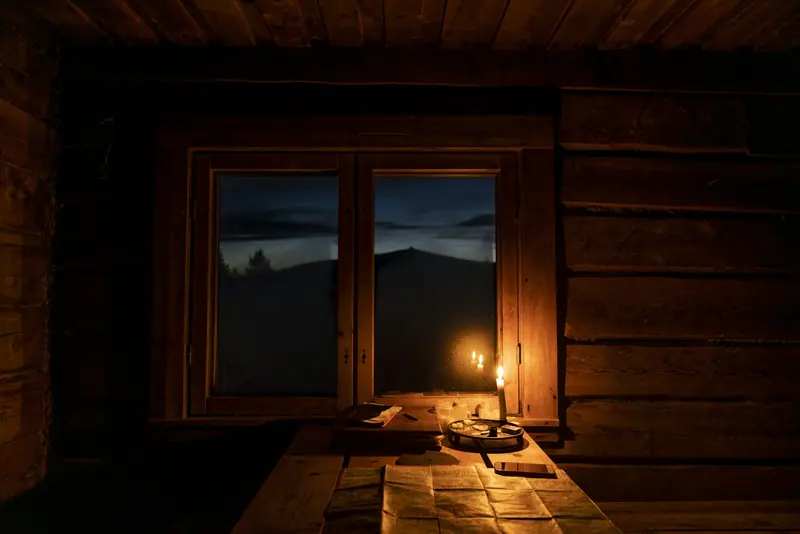 A candle on a cabin table by the window at dusk