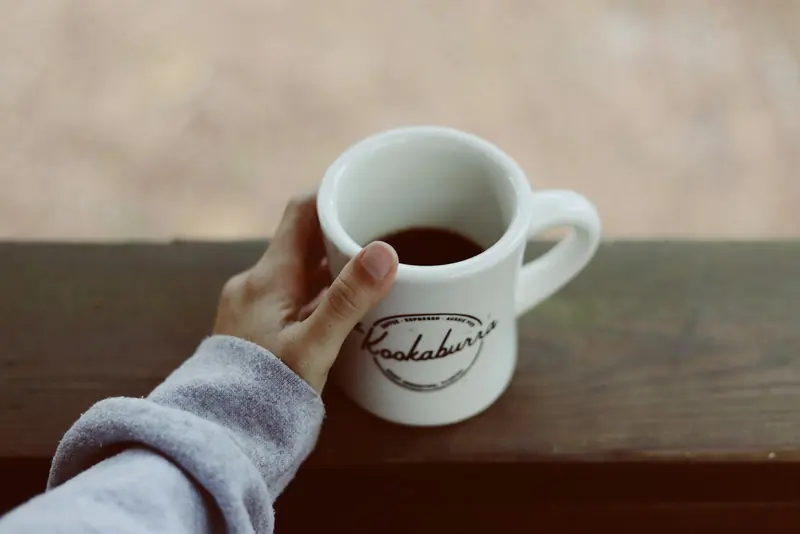 A hand holding a mug of coffee on a porch rail
