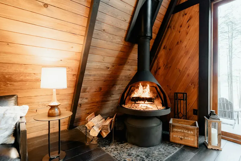 A hanging wood stove glowing inside an A-frame cabin