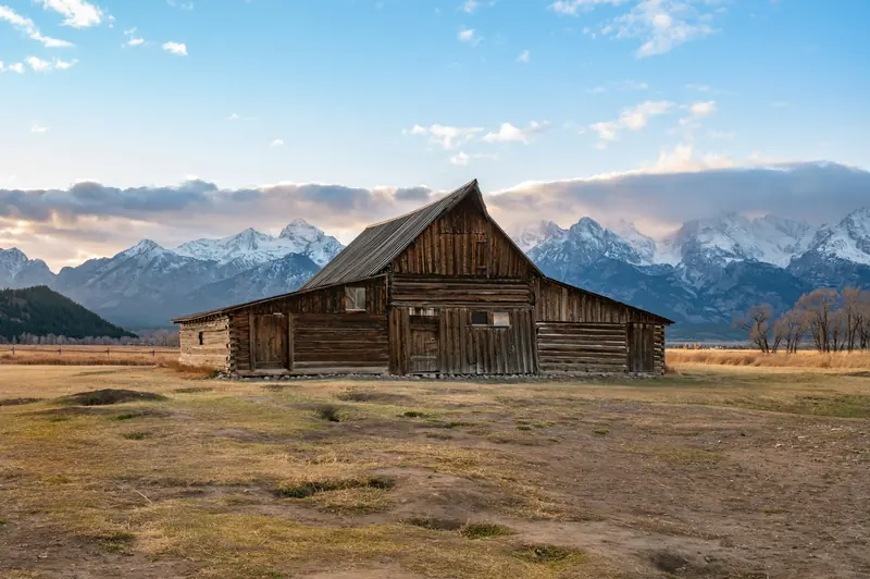 An old log barn on open range below snowy mountains