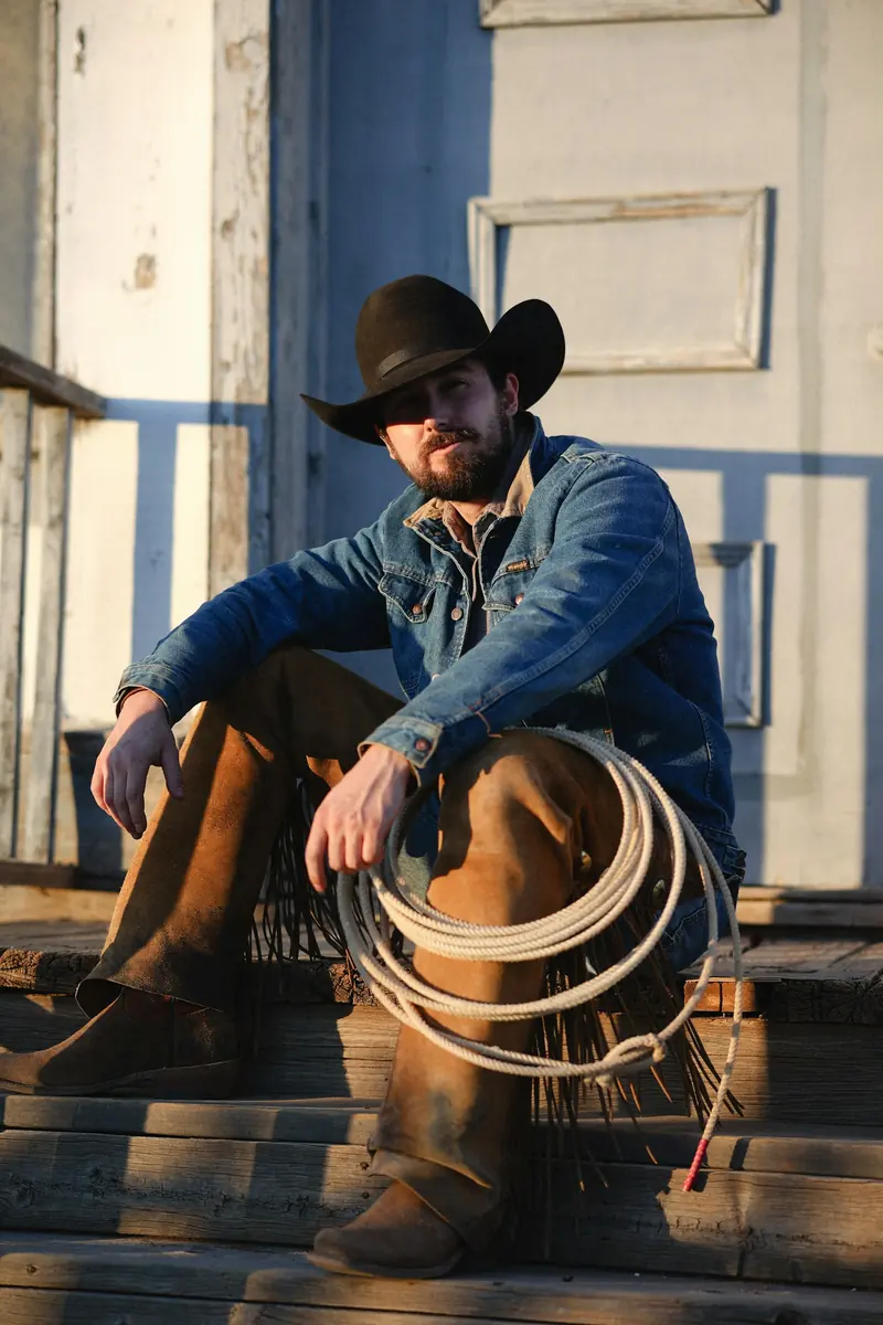 A cowboy sitting on wooden steps with a coiled rope