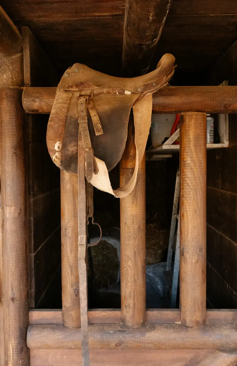 An old leather saddle hanging on a wooden rack in a barn