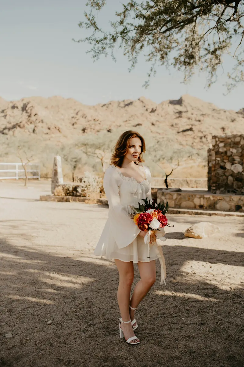 A bride in a short white dress holding flowers in the desert