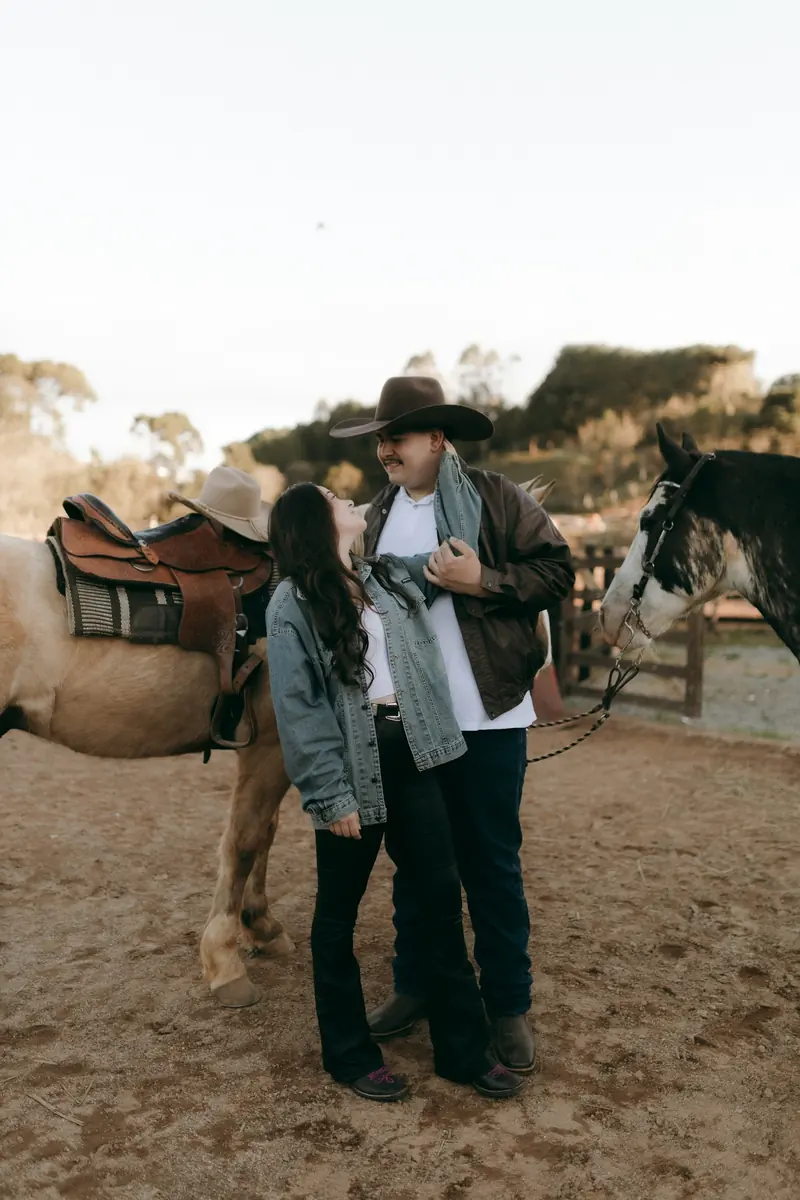 A couple in cowboy hats with their horses in a corral