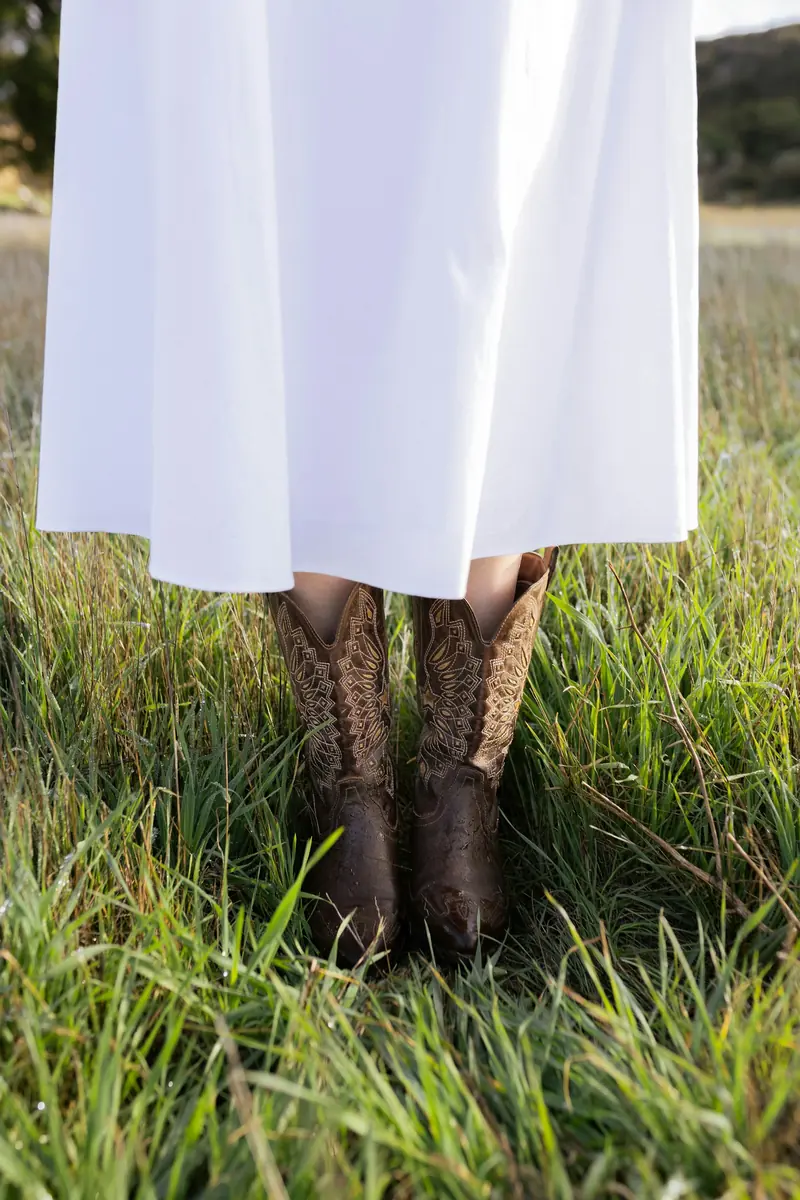 A white dress and brown cowboy boots in green grass