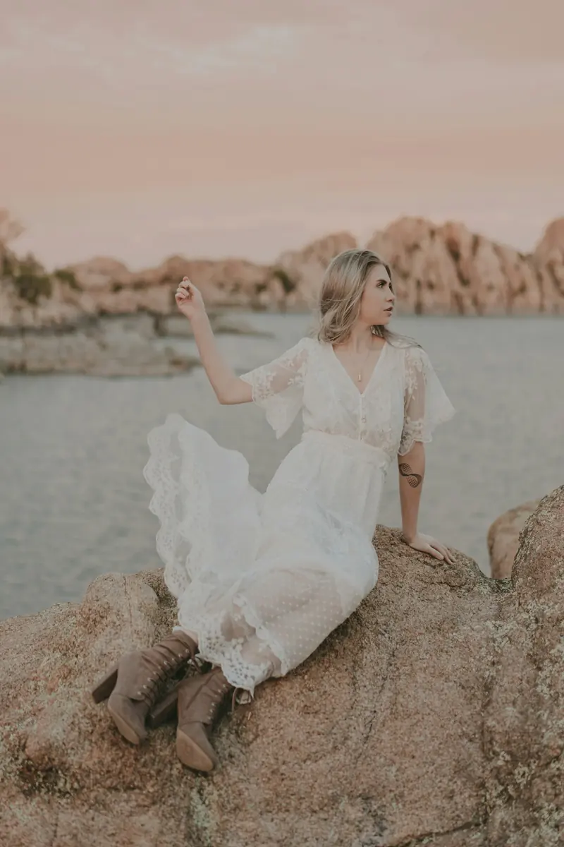 A woman in a white dress laughing on a rock