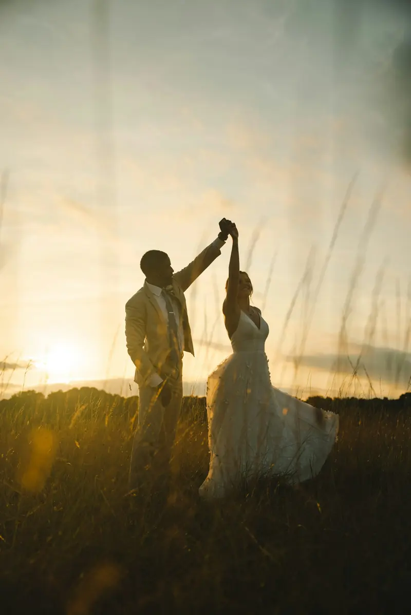 A bride and groom dancing on a ridge at sunset