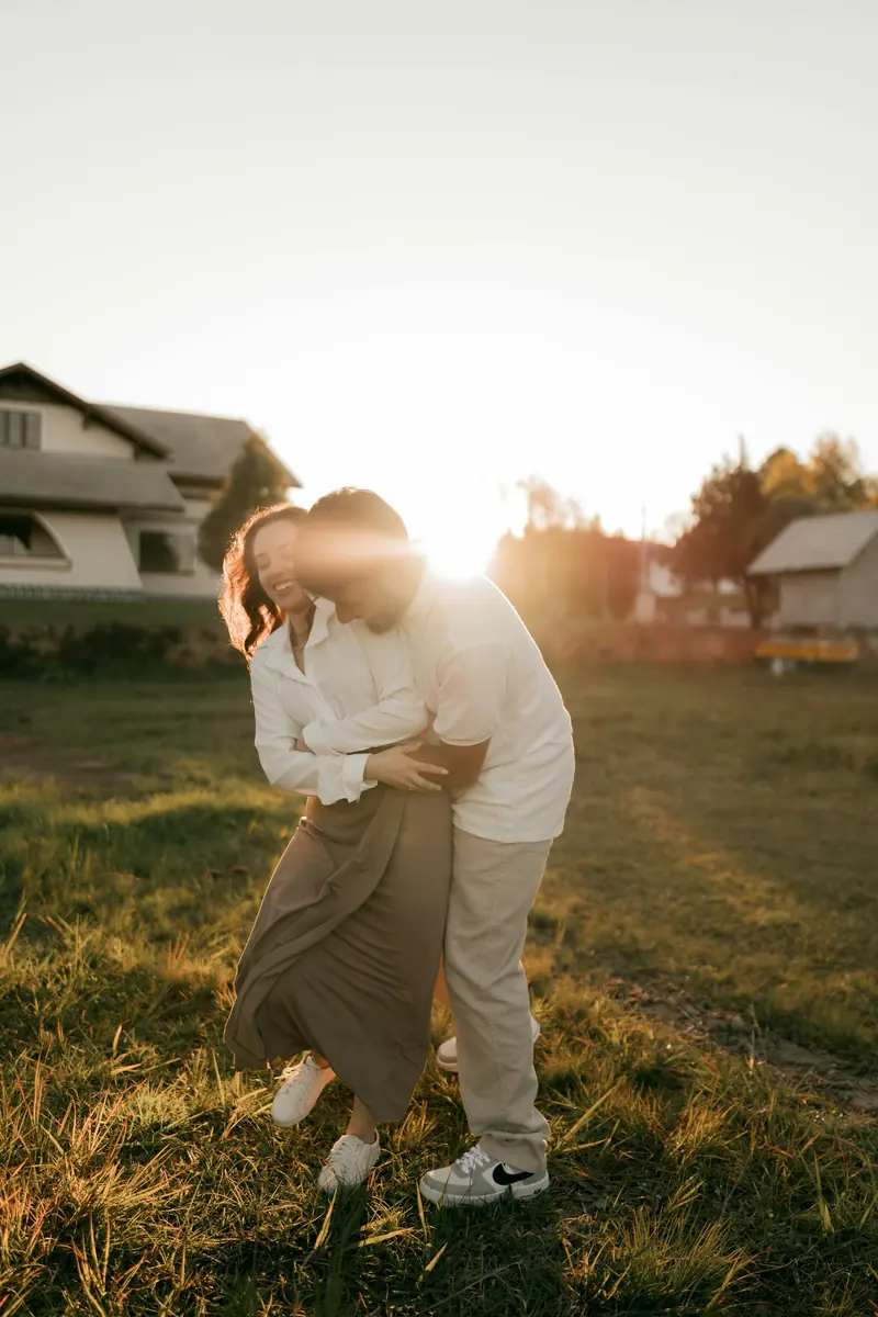 A couple holding each other in a grassy field at sunset
