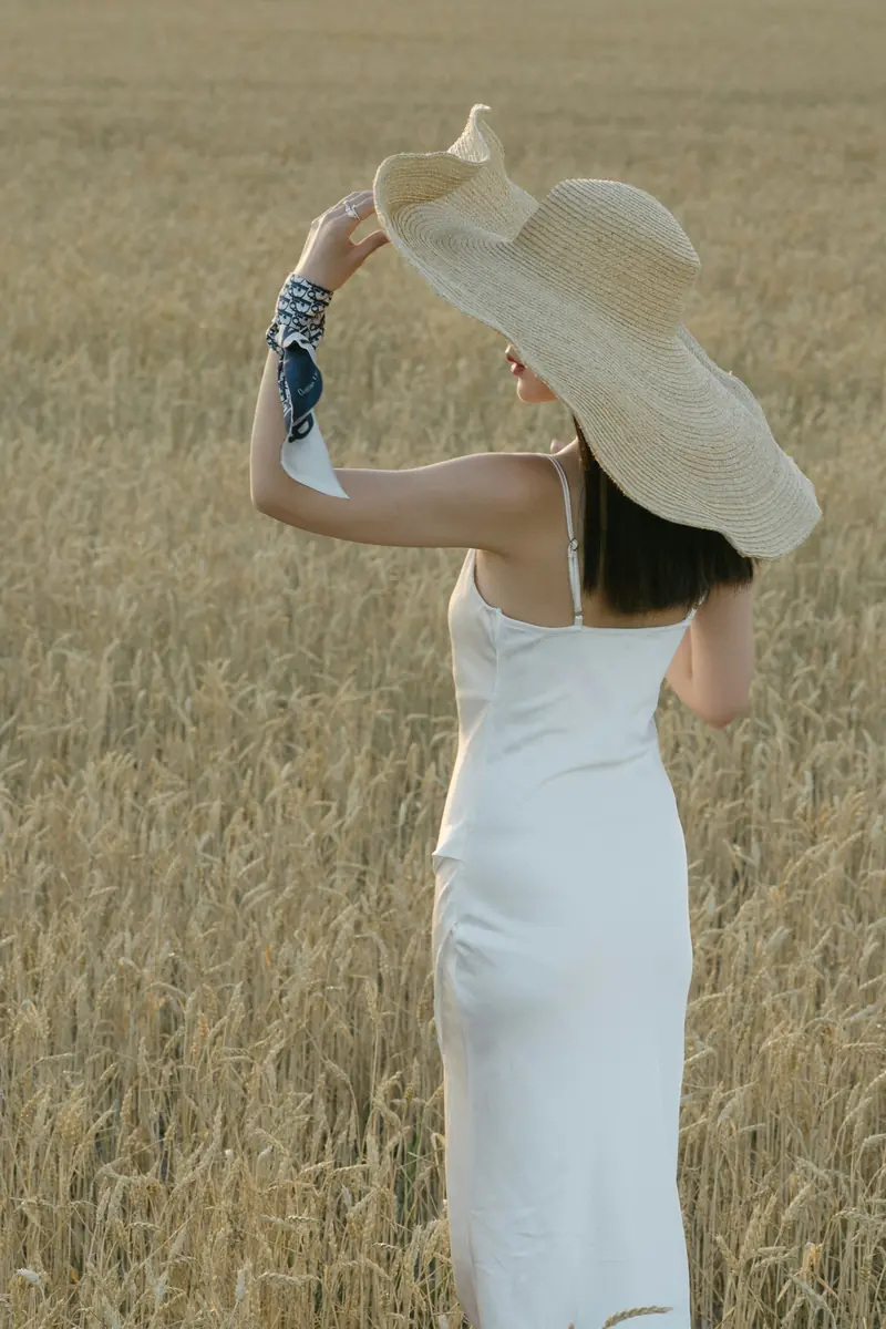 A woman in a white dress and wide hat in dry grass
