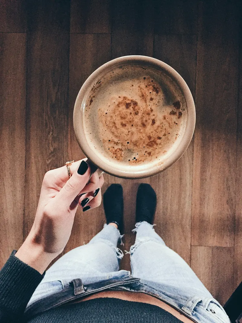A cup of coffee held over faded jeans
