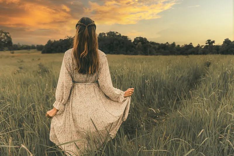 A woman in a white dress walking through a field at sunset