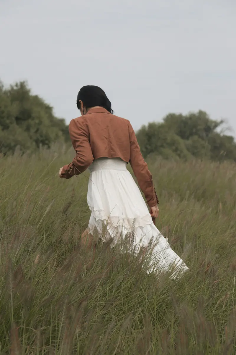 A woman in a white skirt walking through tall grass