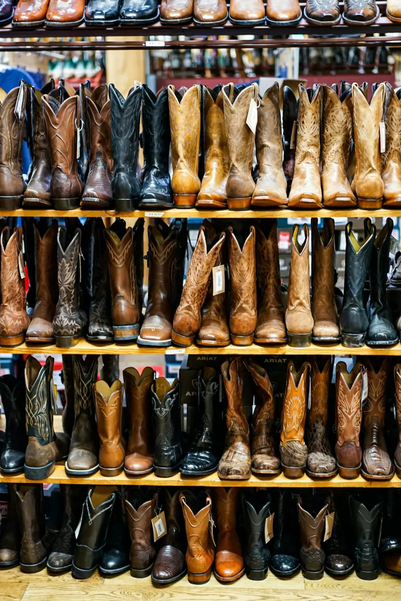 Rows of leather cowboy boots on wooden store shelves